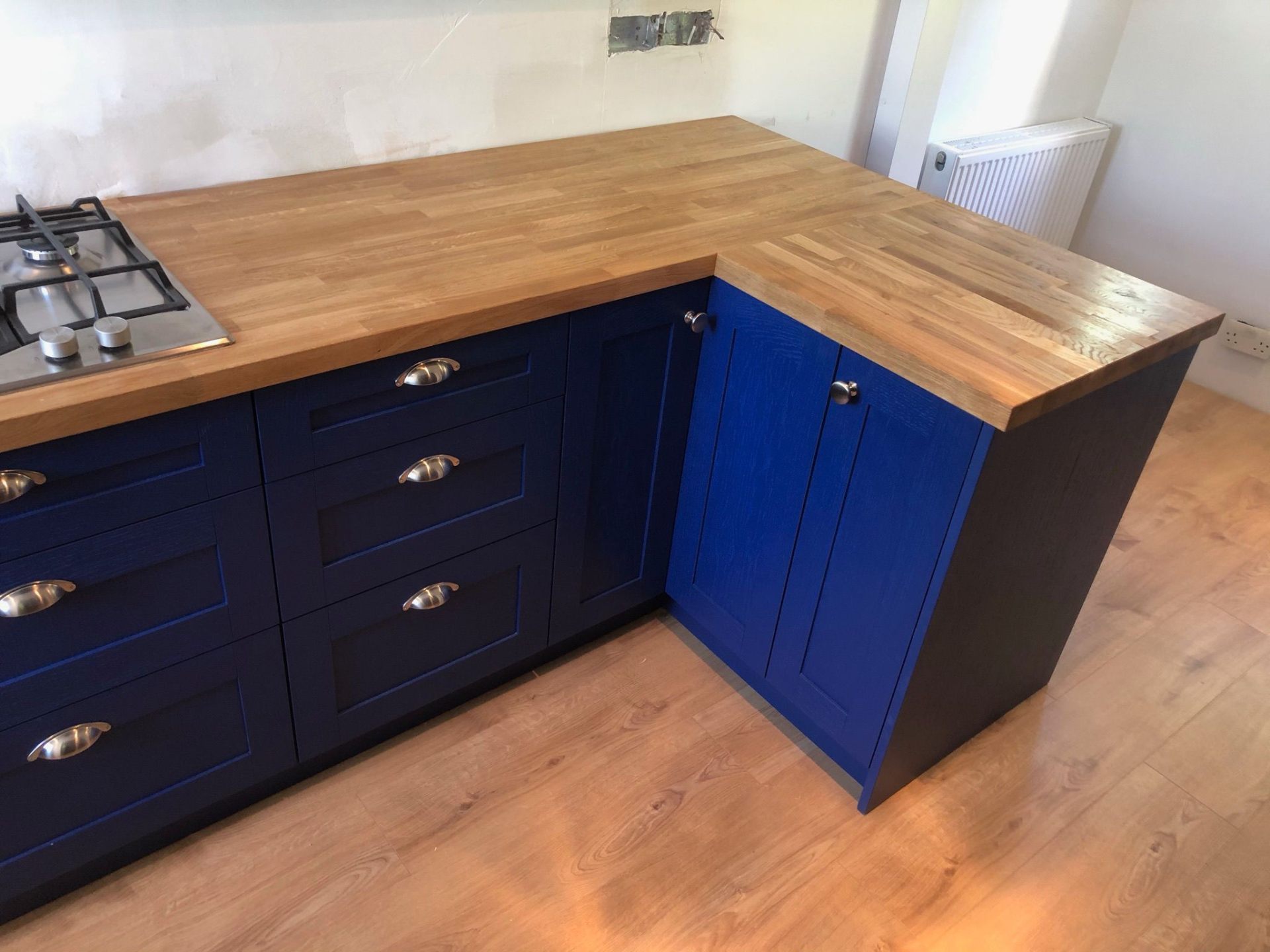 Blue shaker kitchen corner unit with oak worktop and cup handles