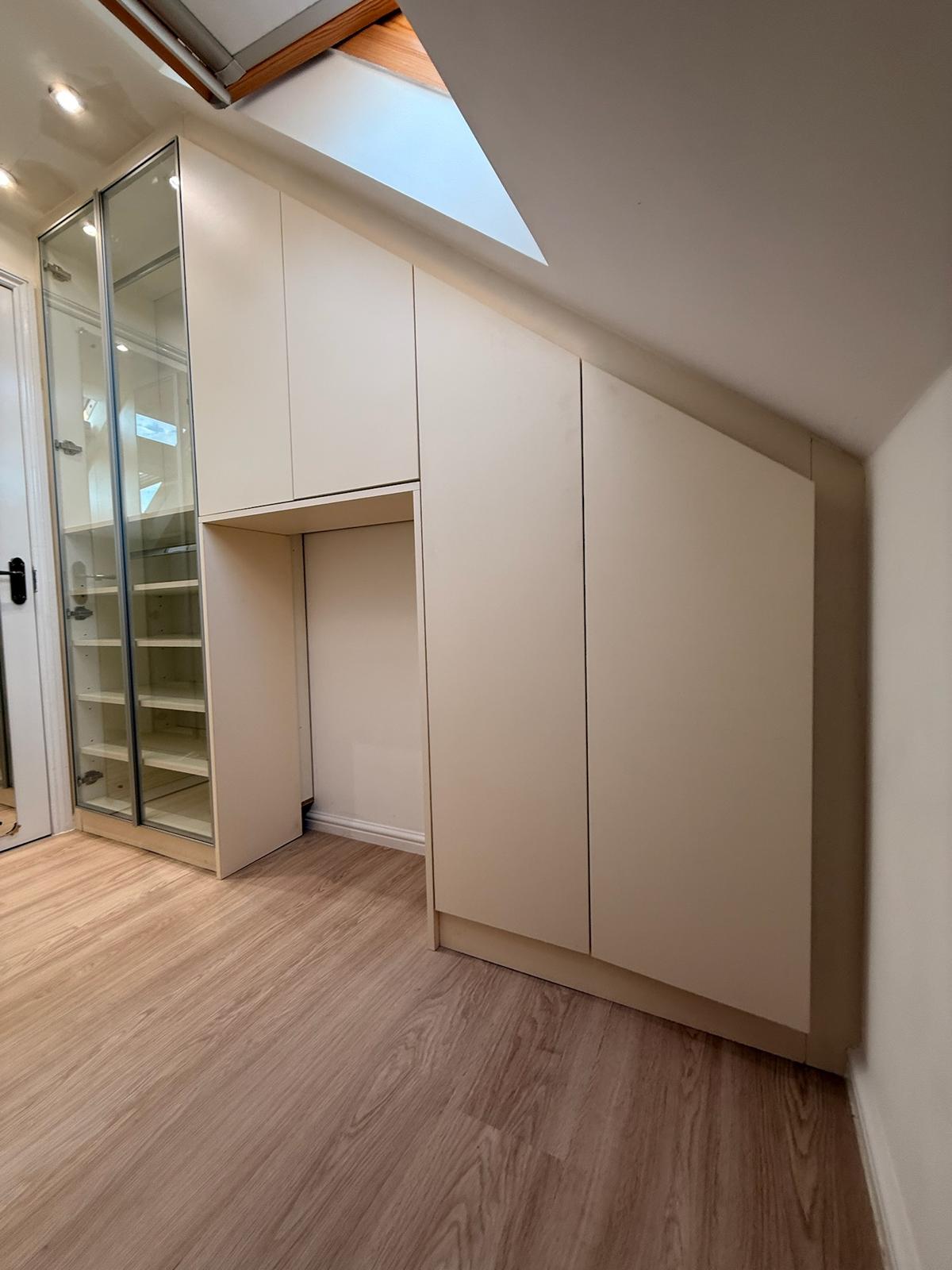 Loft fitted wardrobe with glass cabinet and handleless doors under eaves