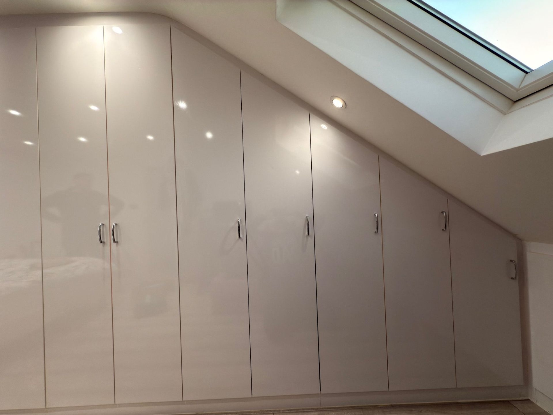 High-gloss white fitted wardrobes following the angle of a loft conversion roof