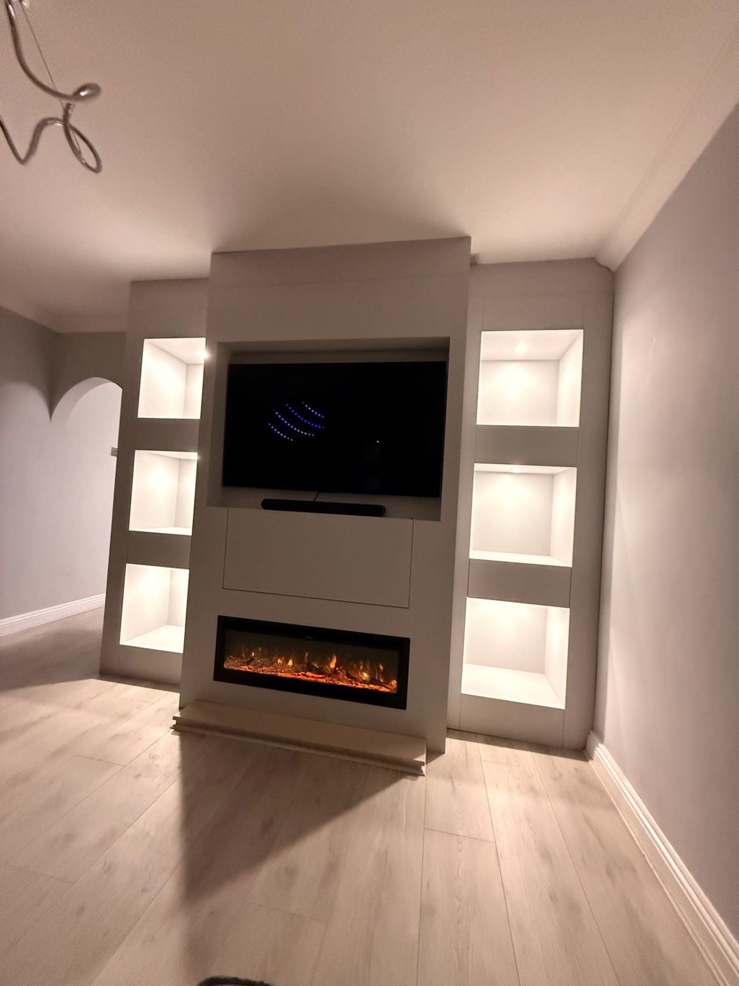 Media wall with electric fireplace and backlit shelving niches in a corner installation