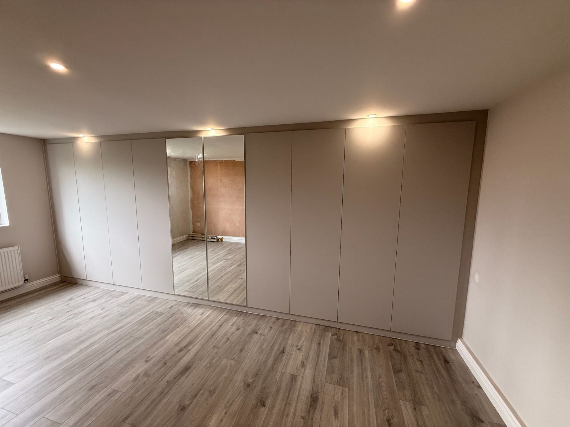 Floor-to-ceiling fitted wardrobes with central mirror panels in a neutral beige finish