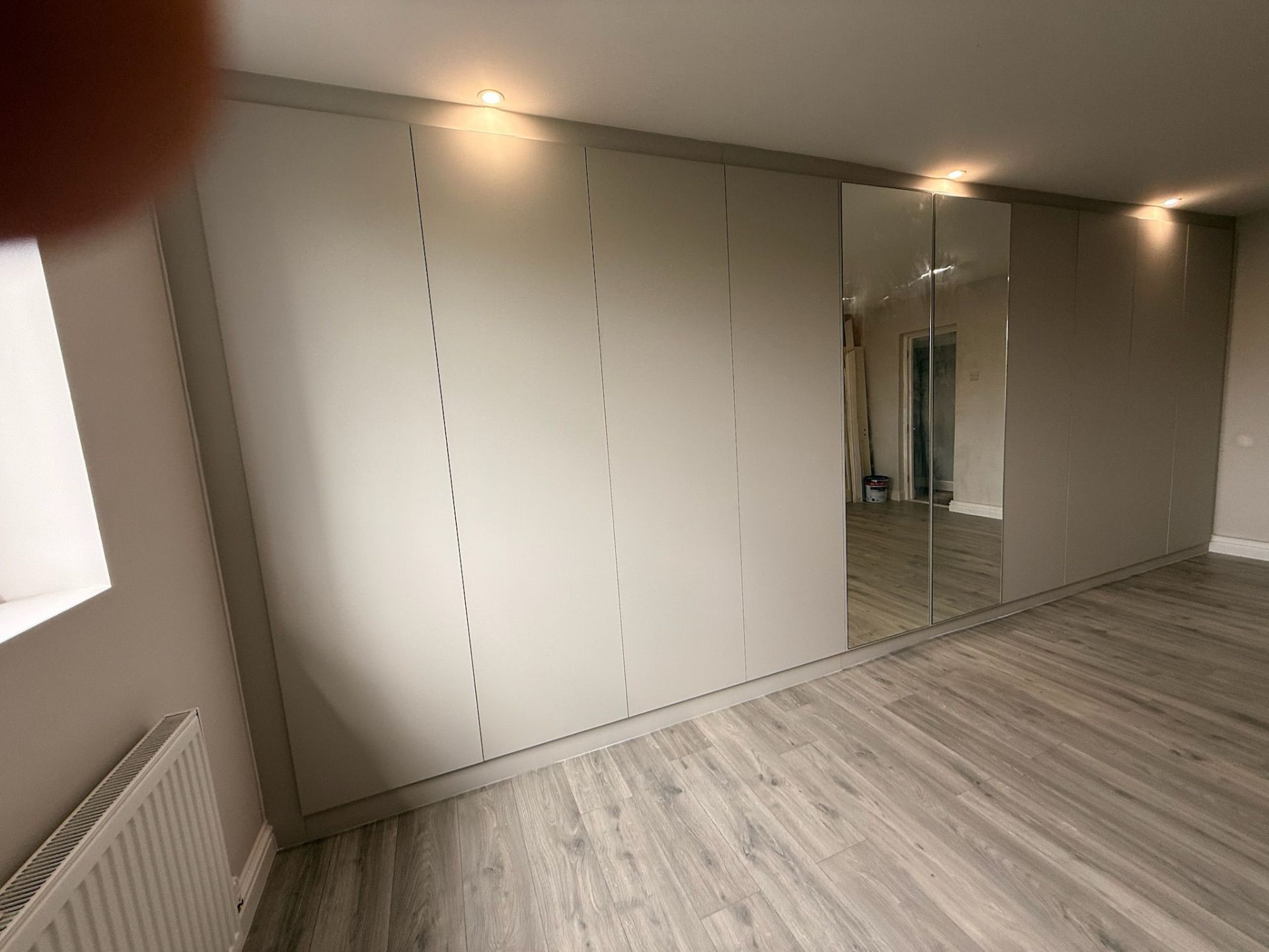Wide fitted wardrobe wall with mirror panels and downlighting