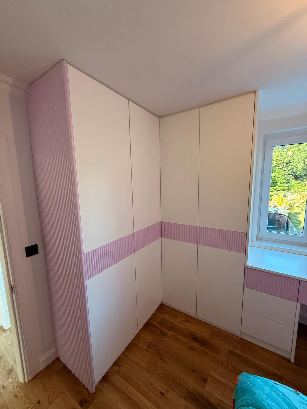 Corner fitted wardrobe in pink fluted panels for a children's bedroom