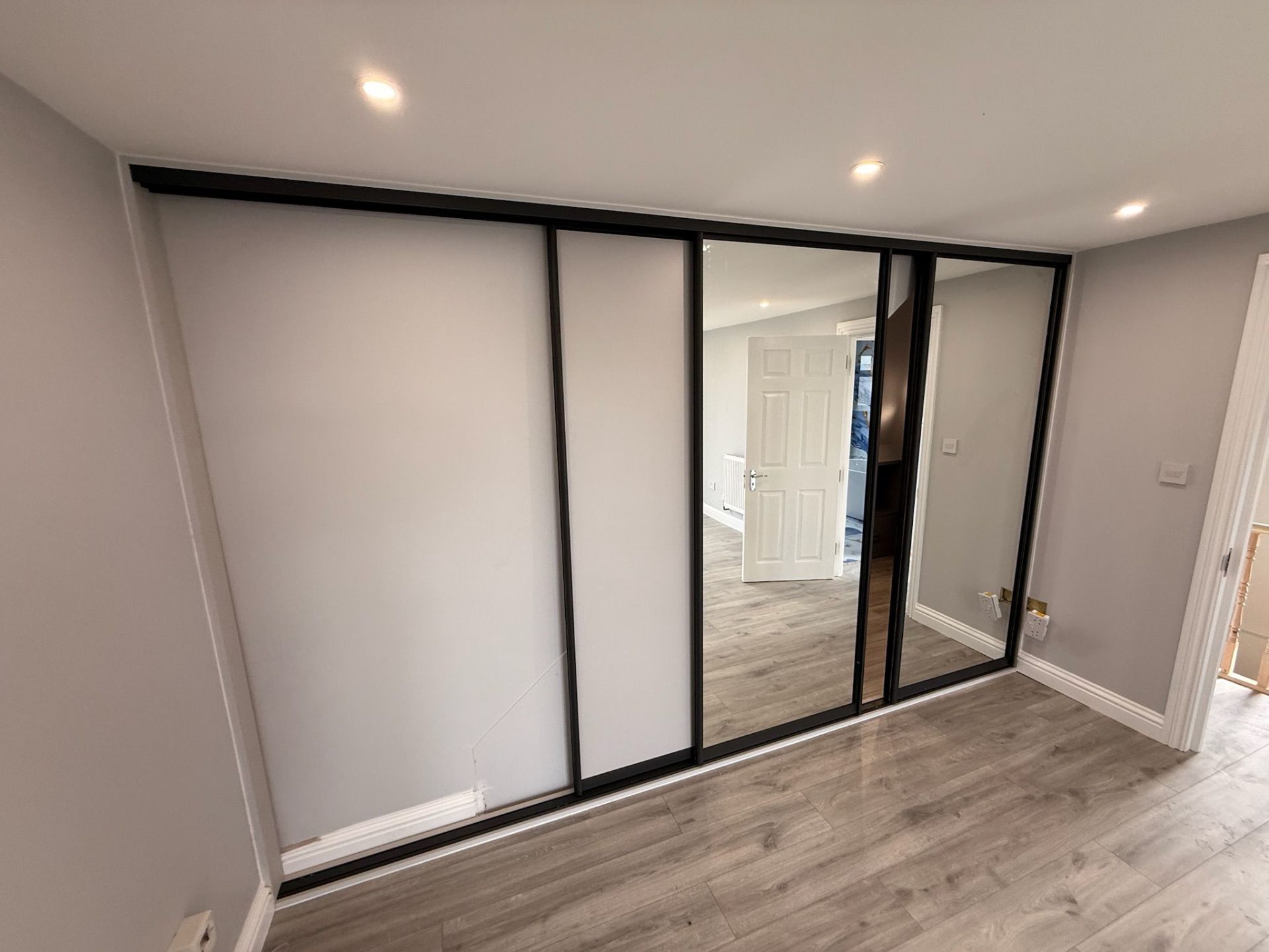 Wide sliding wardrobe with black frame and white panels in a modern bedroom